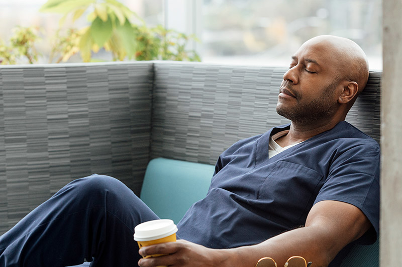 Nurse resting with is eyes closed and sitting down with his coffee
